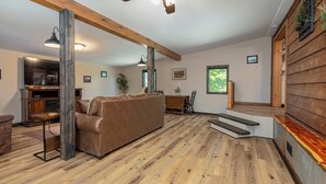 A spacious living room with a brown leather couch, wooden beams, a ceiling fan, and a wooden floor.