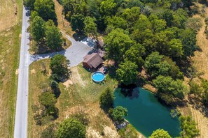 Vista aérea de una casa con piscina, rodeada de árboles frondosos y una pequeña masa de agua.