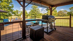 A covered outdoor area with a barbecue grill, a pool table, and a view of a grassy field and trees.