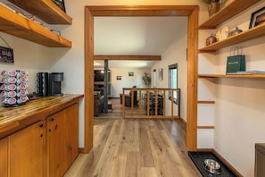 A wooden interior with a kitchen area, a coffee station, and a dining area with a view into the living room.