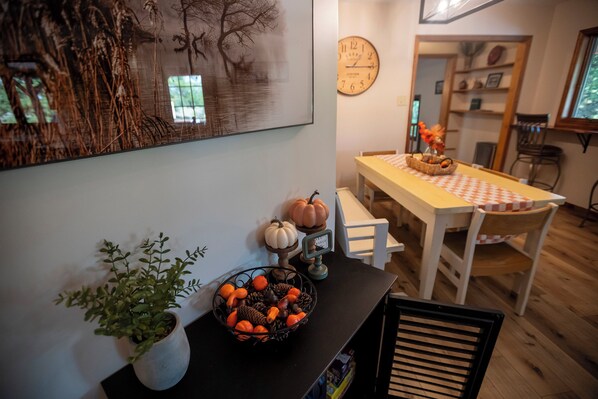 A dining area with a table set for two, a clock on the wall, and a potted plant on a side table. - 5 acre Paradise-Shawnee Wine Trail, Pool, Pond, Firepit, Pet Friendly (Carbondale)