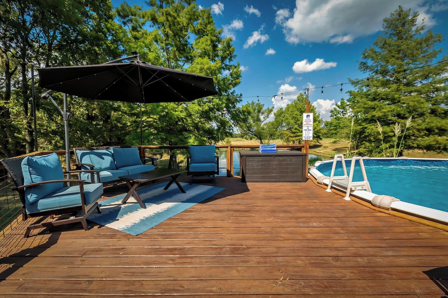 Eine Holzterrasse mit Sitzgelegenheiten im Freien, einem Pool und einem Schild, das einen Kinderspielbereich kennzeichnet.