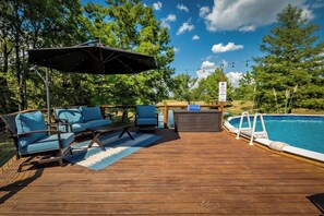 Una terraza de madera con asientos exteriores, una piscina y un letrero que señala un área de juegos para niños.
