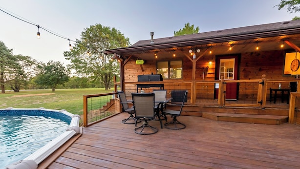 A wooden deck with a pool, outdoor seating, and a barbecue area.