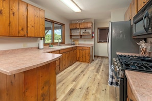 Una cocina con gabinetes de madera, encimera de granito, refrigerador de acero inoxidable y estufa a gas.
