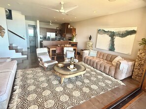 A modern living room with a sofa, armchairs, a coffee table, and a dining area with a kitchen in the background.