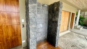 A stone shower enclosure with a wooden floor, adjacent to a wooden door and a staircase leading to an outdoor area.