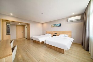 A hotel room with two beds, a desk, and an air conditioning unit.