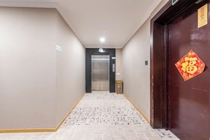 A hallway with a patterned floor, a door with a red decoration, and an elevator in the distance.