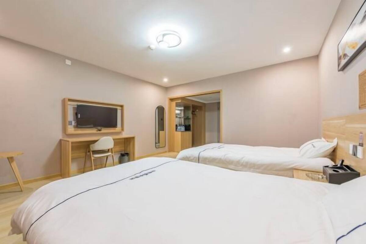 Hotellihuone, jossa on kaksi sänkyä, työpöytä tuolilla, televisio ja peili.