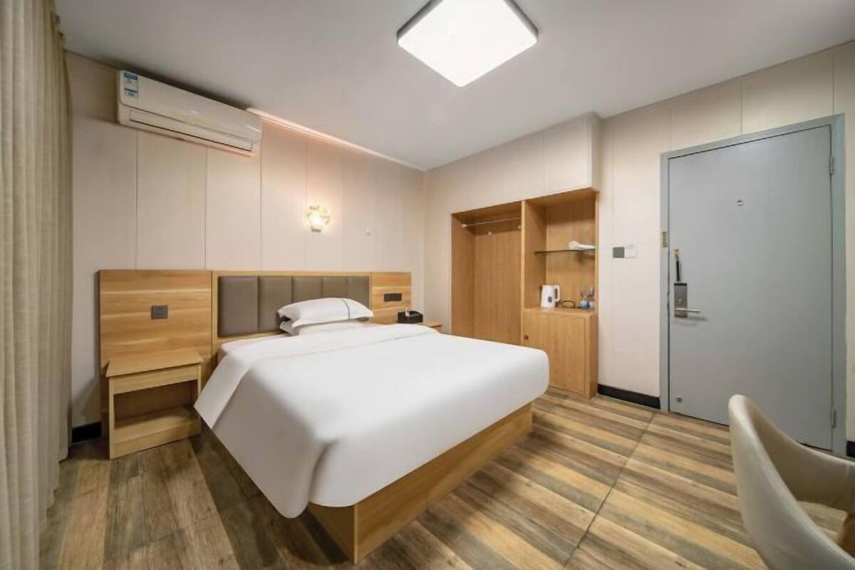 Hotellihuone, jossa on sänky, yöpöytä, vaatekaappi ja tuoli.