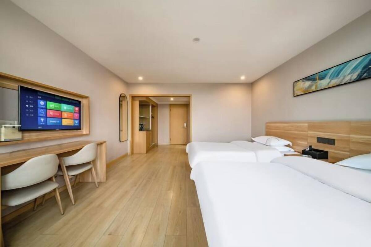 Hotellihuone, jossa on työpöytä, kaksi sänkyä, televisio ja taulu seinällä.