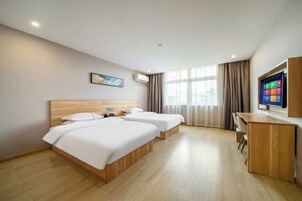 A hotel room with two beds, a desk, a TV, and large windows.