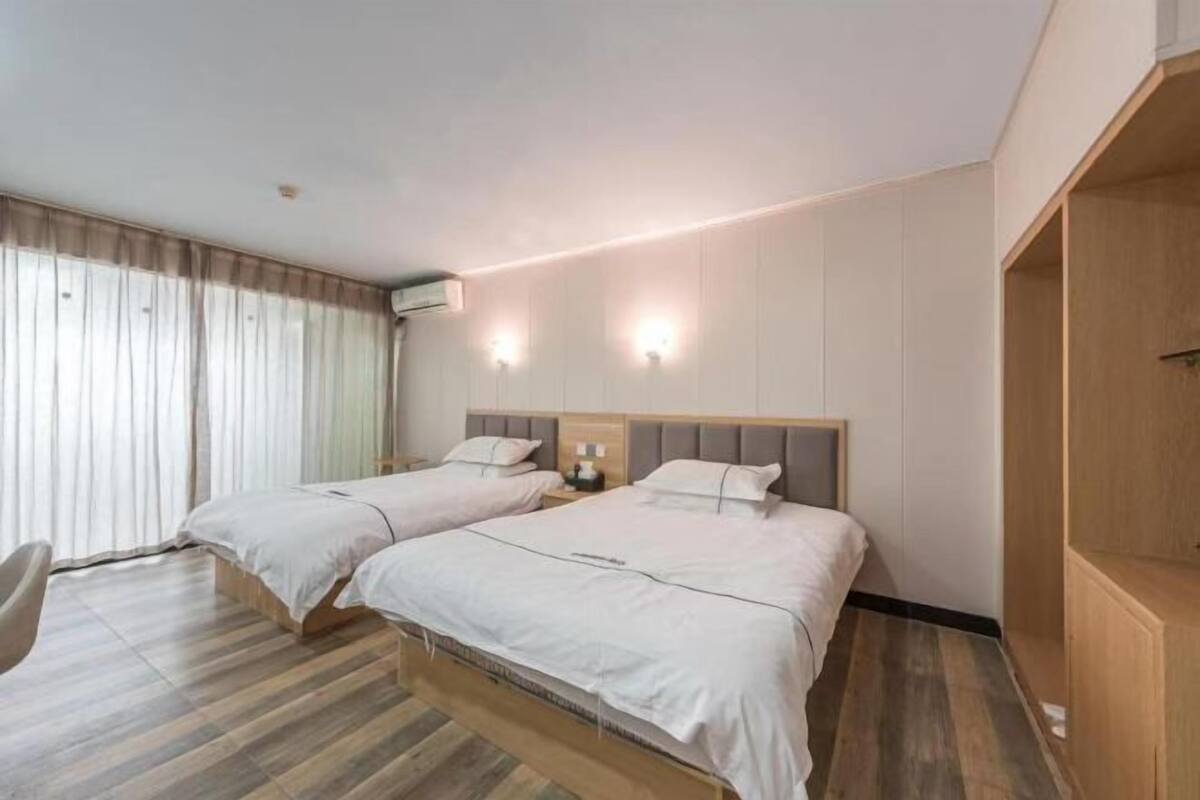 Hotellihuone, jossa on kaksi sänkyä, puinen vaatekaappi, työpöytä ja tuoli.
