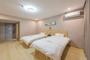 Habitación de hotel con dos camas, cabecero de madera, unidad de aire acondicionado, un cuadro en la pared y una puerta que da a otra habitación.