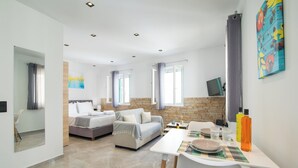 A modern hotel room with a bed, a sofa, a dining table, and a TV. - Little Gem by Corfu Escapes (Corfu)