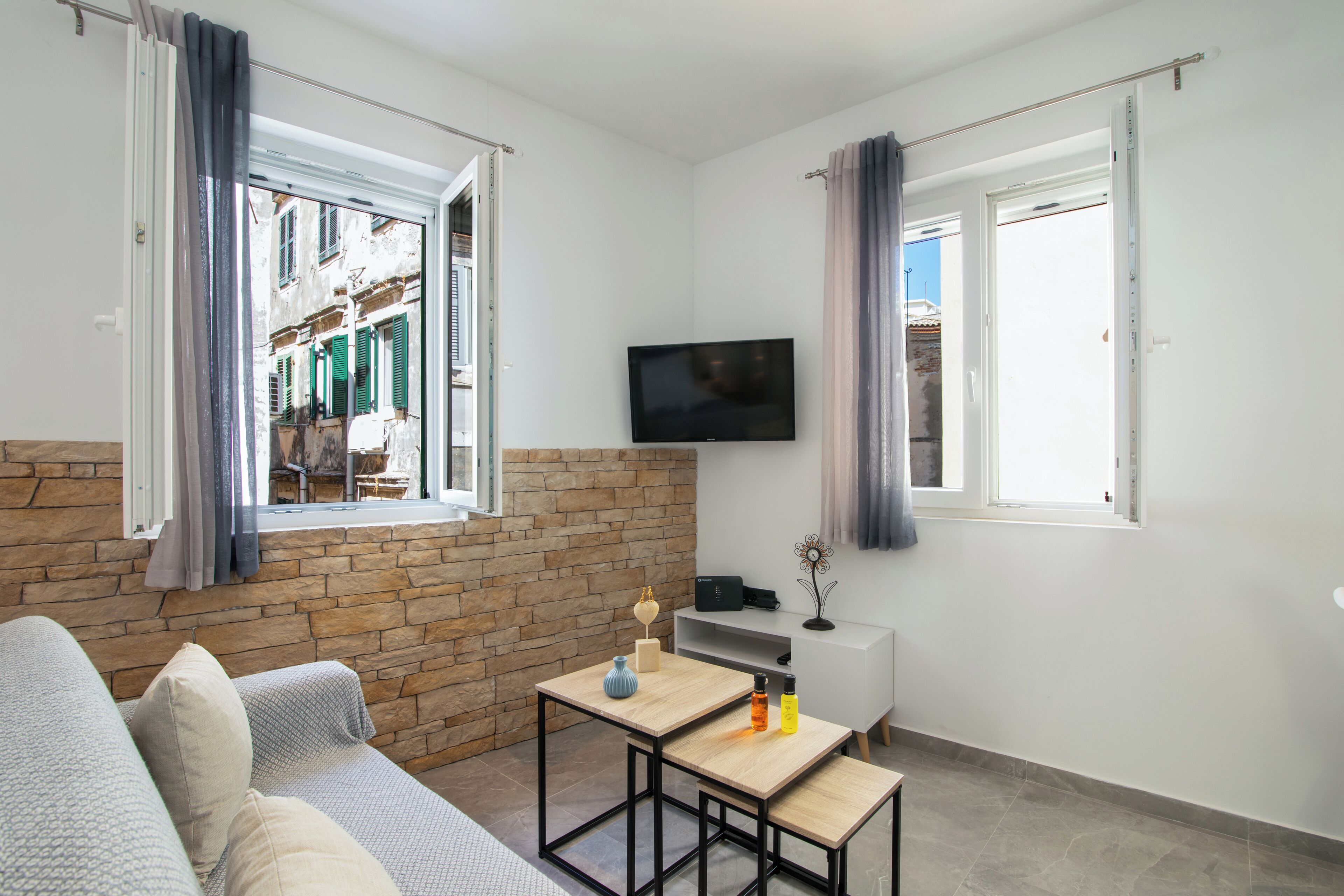 A modern living room with a stone wall, a sofa, a TV, and a table with a lamp and bottles.