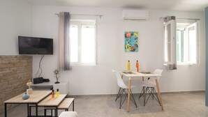 A modern living room with a flat-screen TV, a dining table with chairs, a fireplace, and a painting on the wall. - Little Gem by Corfu Escapes (Corfu)
