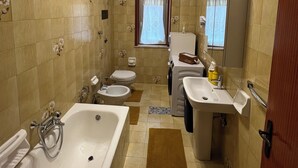 A bathroom with a bathtub, two sinks, a toilet, and a washing machine. - Uncle Peppino Holiday House (Torregrotta)