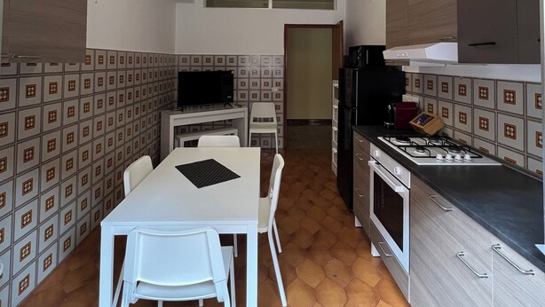 A compact kitchen with a dining area, featuring a white table and chairs, a gas stove, and a microwave. - Uncle Peppino Holiday House (Torregrotta)