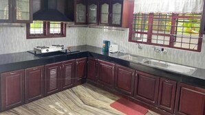 A kitchen with dark wooden cabinets, a black countertop, a gas stove, a sink, and a window with a view of greenery.