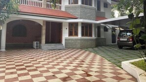 A two-story house with a checkered floor pattern, a balcony, and a car parked in the driveway.