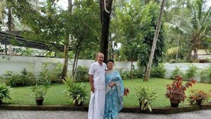 Two people standing in a garden with potted plants and a paved walkway.
