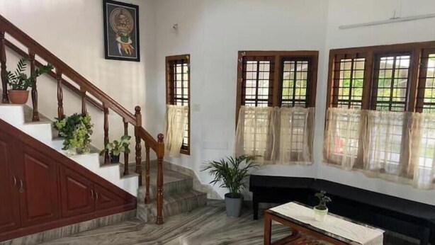 A staircase with wooden railings and potted plants, a marble floor, a bench, and windows with curtains.
