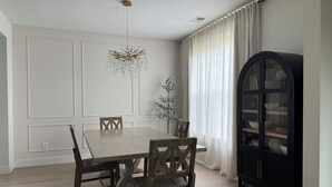 A dining room with a wooden table and chairs, a chandelier, a cabinet with glass doors, and a window with curtains.