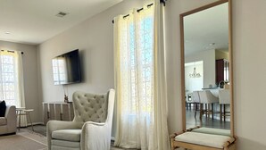 A spacious living room with a large mirror, a comfortable armchair, and a wooden floor.