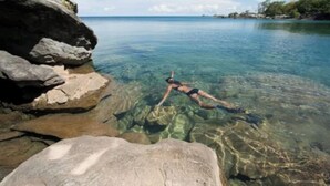 Une personne faisant de la plongée avec tuba dans une eau claire, près de gros rochers.
