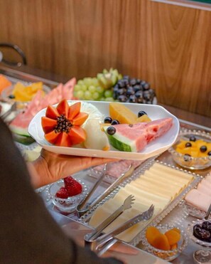 A plate of assorted fruits and cheeses, with a wooden background. - Hotel Imperatriz Premium (Telemaco Borba)