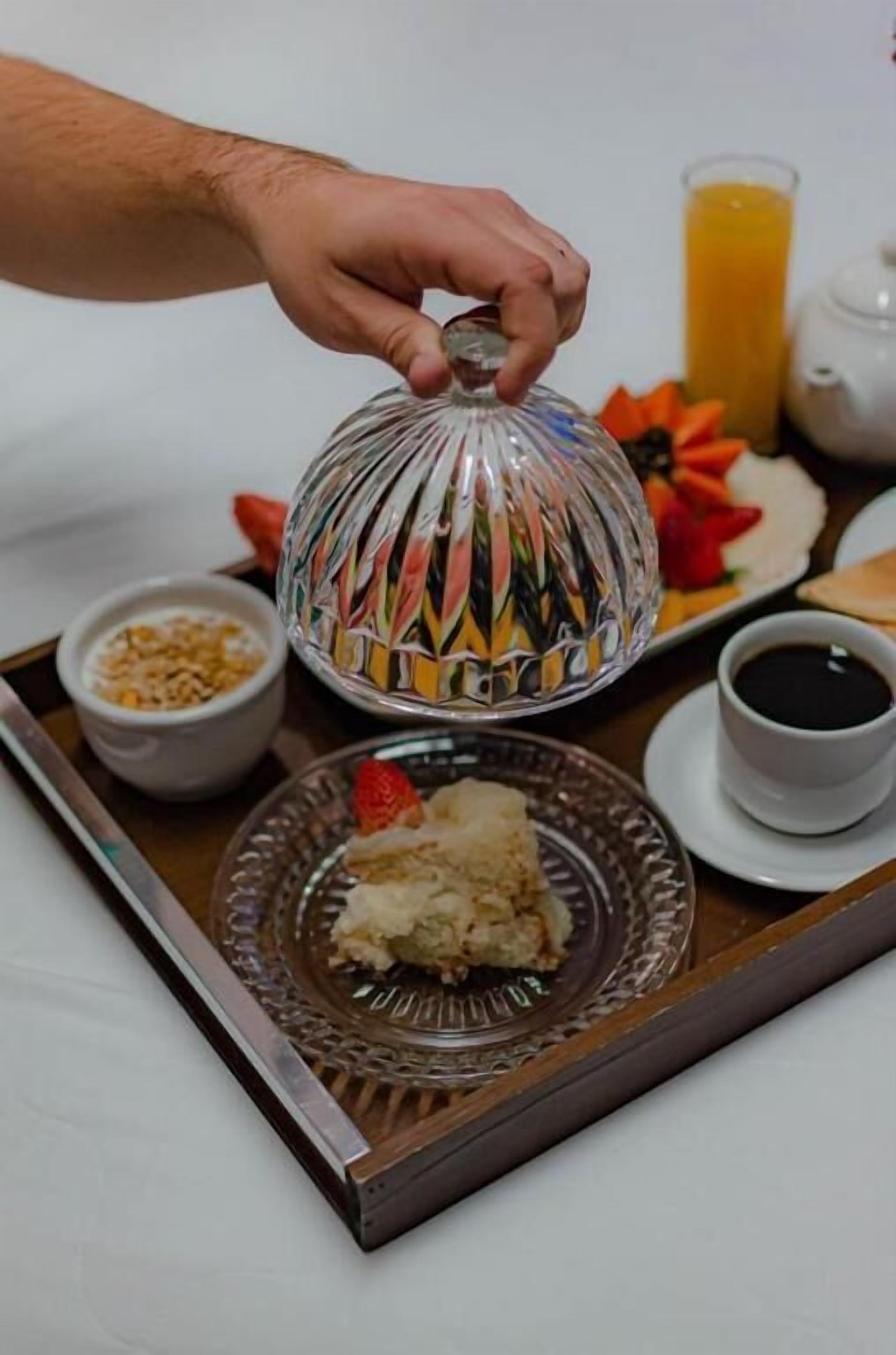 A breakfast tray with a glass dome cover, a cup of coffee, a glass of orange juice, and a plate with food.