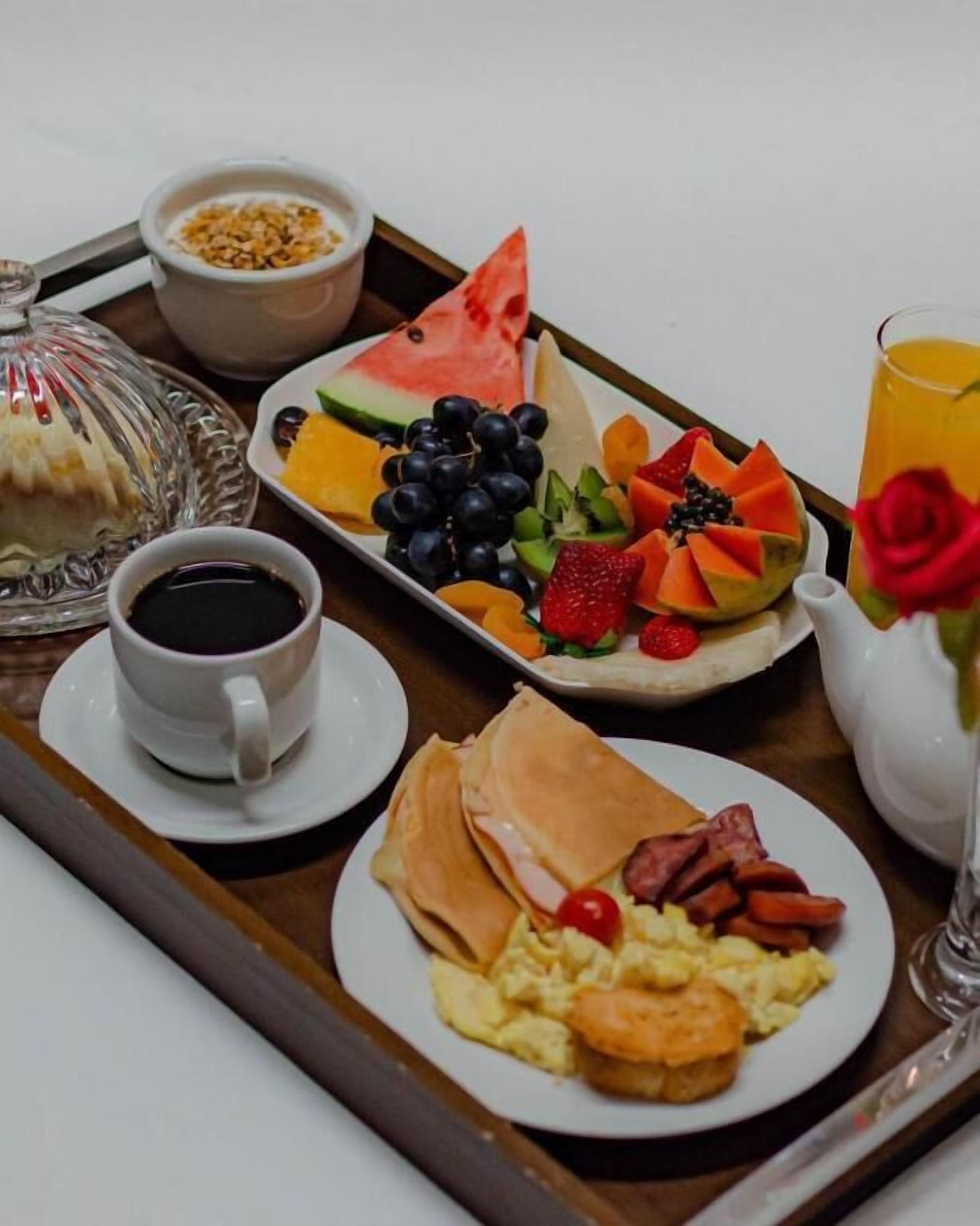 A breakfast tray with a variety of foods including pancakes, scrambled eggs, sausages, and a selection of fruits and vegetables.