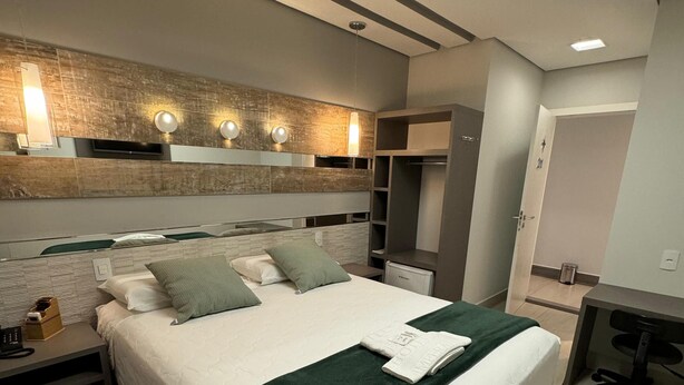 A modern bedroom with a large bed, bedside tables, a desk, and built-in wardrobe. - Hotel Imperatriz Premium (Telemaco Borba)