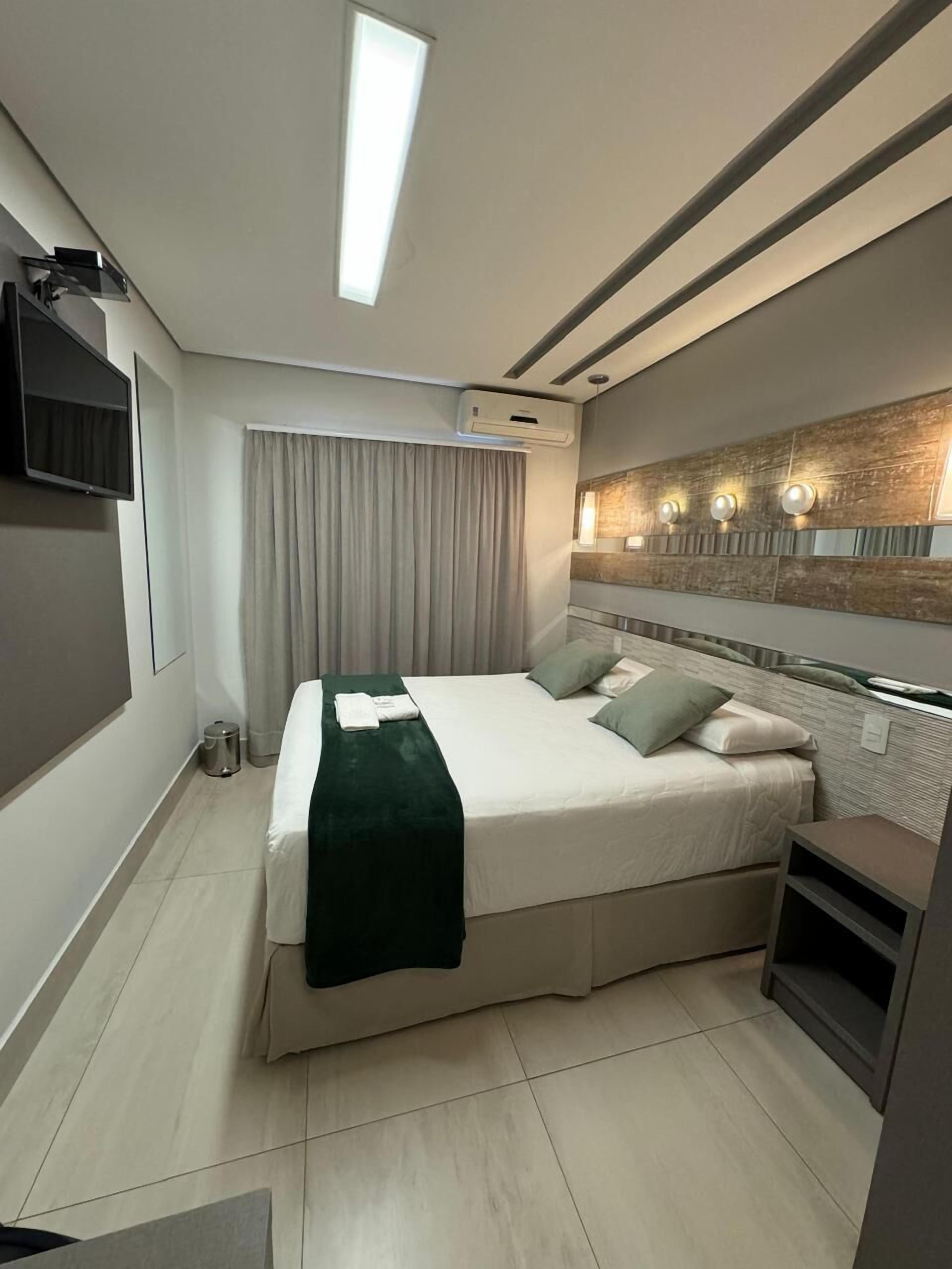 Une chambre d’hôtel moderne dotée d’un grand lit, d’une télévision, d’un système de climatisation et d’une salle de bain avec un miroir et des luminaires.
