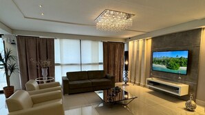 A modern living room with a flat-screen TV, a chandelier, a sofa, and a coffee table. - Hotel Imperatriz Premium (Telemaco Borba)