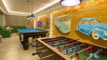 Um quarto com mesa de pebolim, mesa de bilhar e um mural de carros antigos.