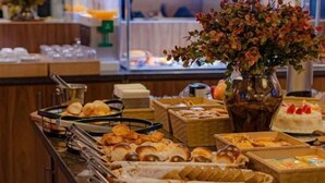 A buffet with various food items and a vase of flowers. - Hotel Imperatriz Premium (Telemaco Borba)