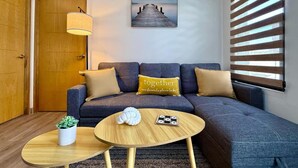 A modern living room with a sofa, two round wooden tables, a potted plant, and a wall-mounted lamp. - Condo a 3 blocks from La Paz Malecon (La Paz)