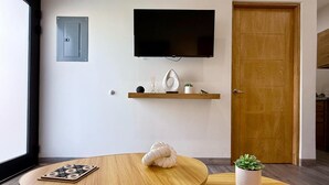 A modern living room with a flat-screen TV mounted on the wall, a wooden door, and a small shelf with decorative items. - Condo a 3 blocks from La Paz Malecon (La Paz)