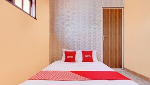 A hotel room with a bed, two red pillows, a red and white patterned blanket, and a wooden door. - Hotel O Griya Mustika Syariah (Ngemplak)