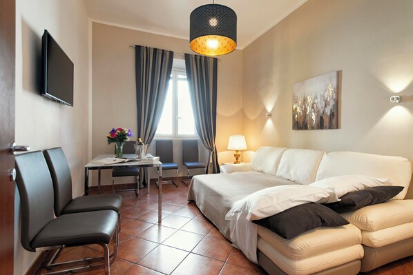 A hotel room with a bed, a sofa, a desk with a chair, a TV, a lamp, and a painting on the wall. - Veneto Prestige Apartment  (Rome)