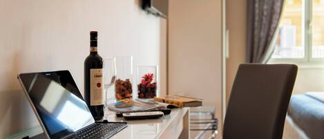A laptop on a glass desk with a bottle of wine, a remote control, and a magazine.