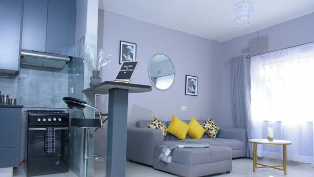 Una sala de estar moderna con un sofá gris, una mesita redonda y una zona de cocina con estufa y horno.