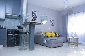 A modern living room with a grey sofa, a small round table, and a kitchen area with a stove and oven. - Gorgeous City Apartment in Harare Avenues, cbd (Harare)