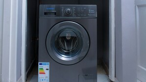 Un lavadero pequeño y moderno con lavadora integrada y un armario gris arriba.