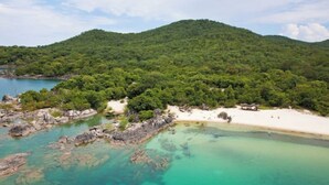 A coastal landscape with a beach, clear turquoise waters, and a forested hill. - Nkwichi Lodge, self-catering luxury chalet Niassa B

 (Matola)