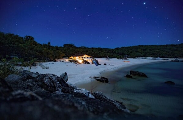 A beach with a building on the shore, surrounded by trees and rocks. - Nkwichi Lodge, self-catering luxury chalet Niassa B

 (Matola)