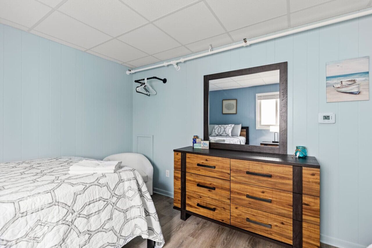 A bedroom with a bed, a wooden dresser, a mirror, and a wall-mounted bicycle rack.